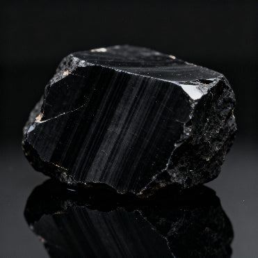 raw black onyx stone with natural vertical bands and glossy texture on dark reflective background
